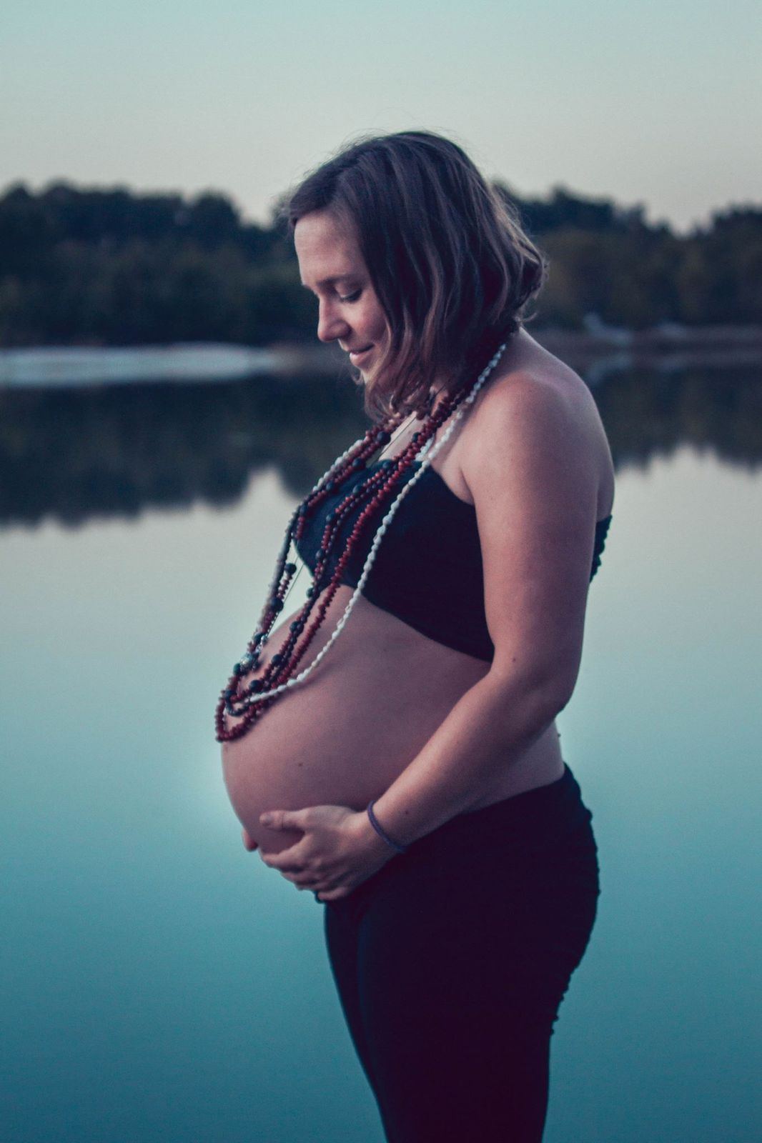 Hannah Stiegler enceinte au bord d'un lac au crépuscule, les mains sur le ventre